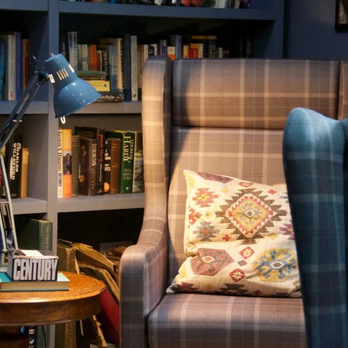 A closeup of a tartan armchair and reading lamp in the library.