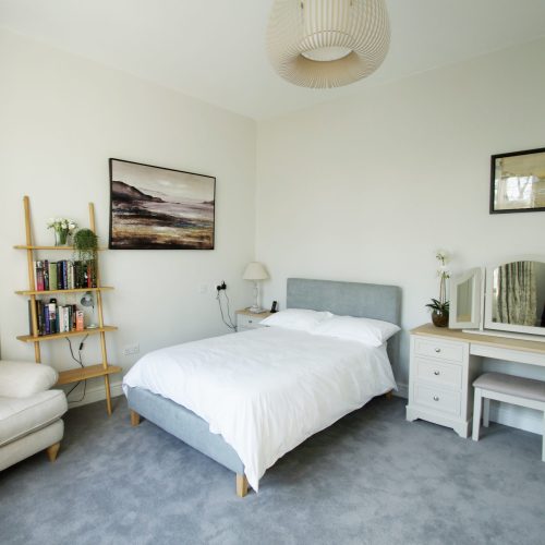Picture of a respite room with bed, comfy armchair and dressing table, in shades of cream and grey.